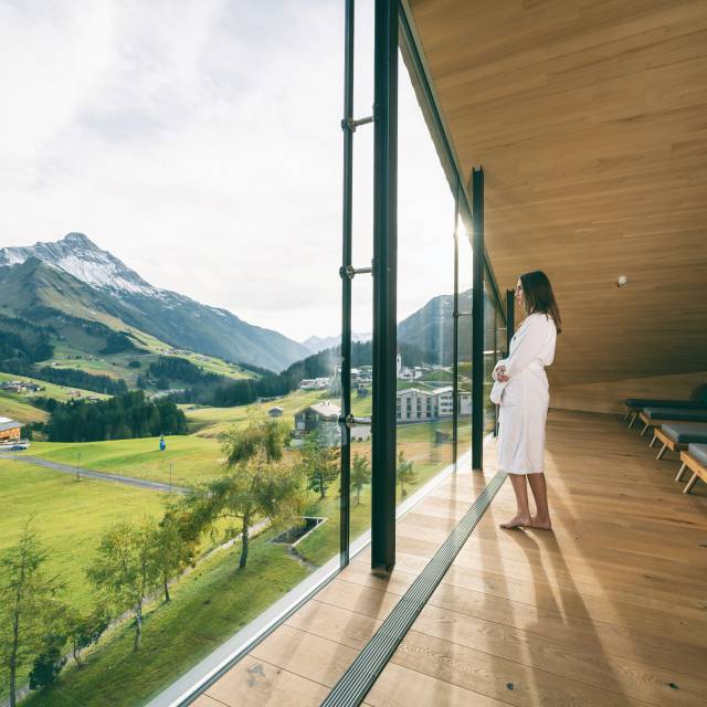 Frau blickt aus Fenster mit Aussicht auf den Arlberg