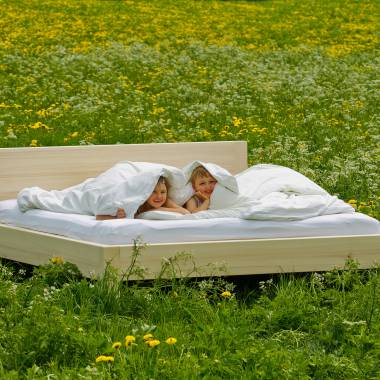 Natürliches Bettgestell mit Matratze auf grüner Wiese mit Kindern