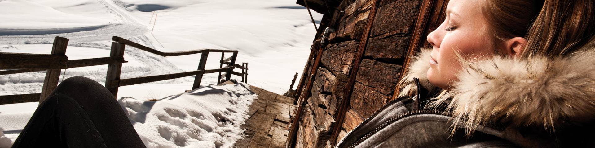 Frau genießt die Sonne vor einer Berghütte im Winter