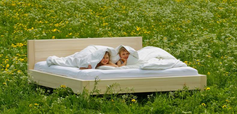 Kinder liegen in Doppelbett auf einer Blumenwiese