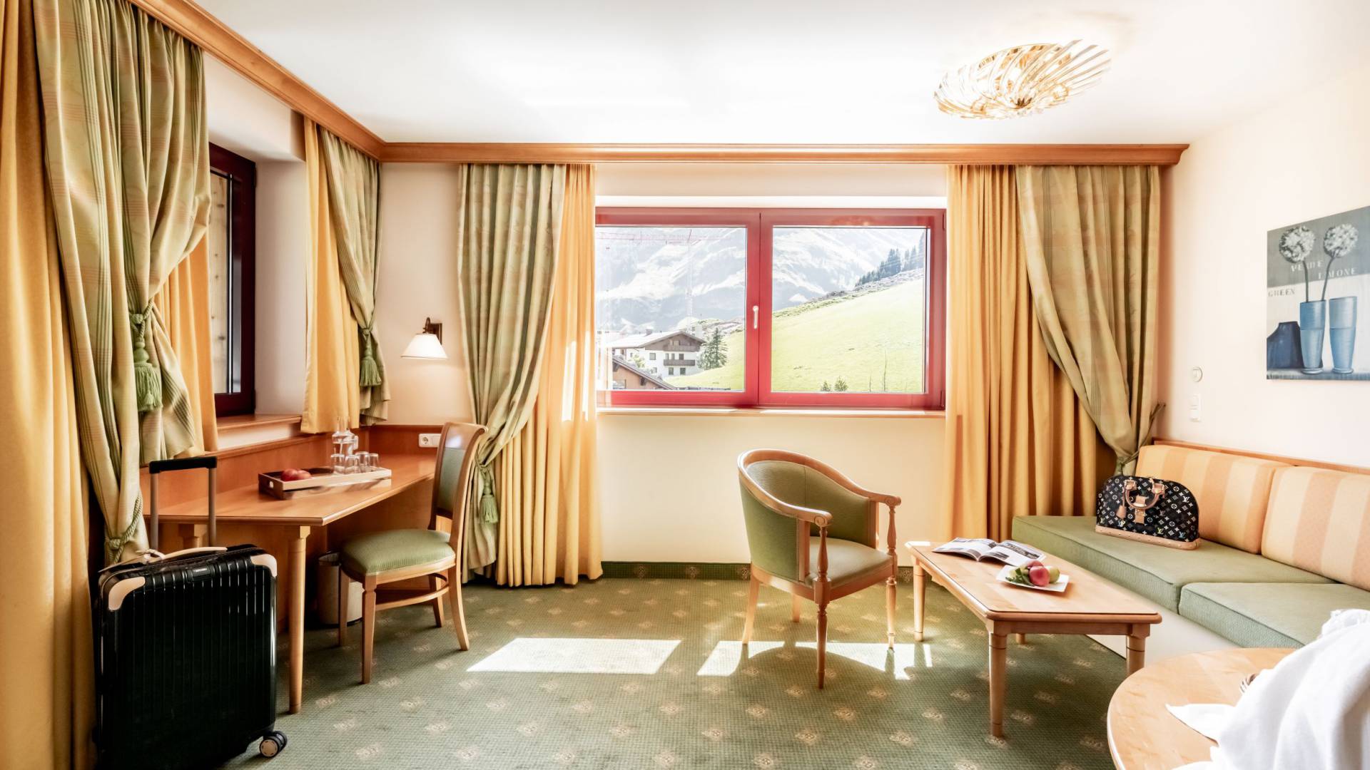 Rustic-style hotel room with green carpet and light-colored walls. There is also a desk and a seating area.