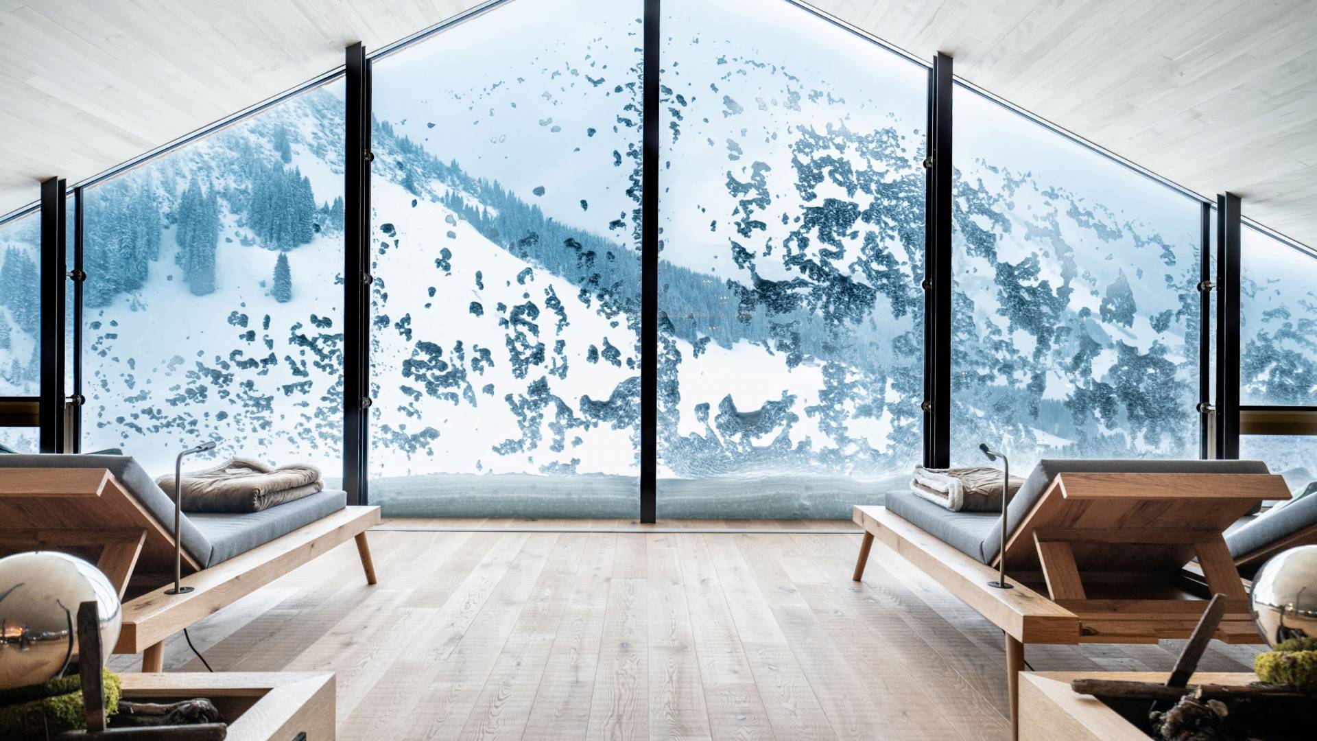 Panorama-Ruheraum mit stilvollen Liegen und verschneitem Alpenblick am Arlberg.